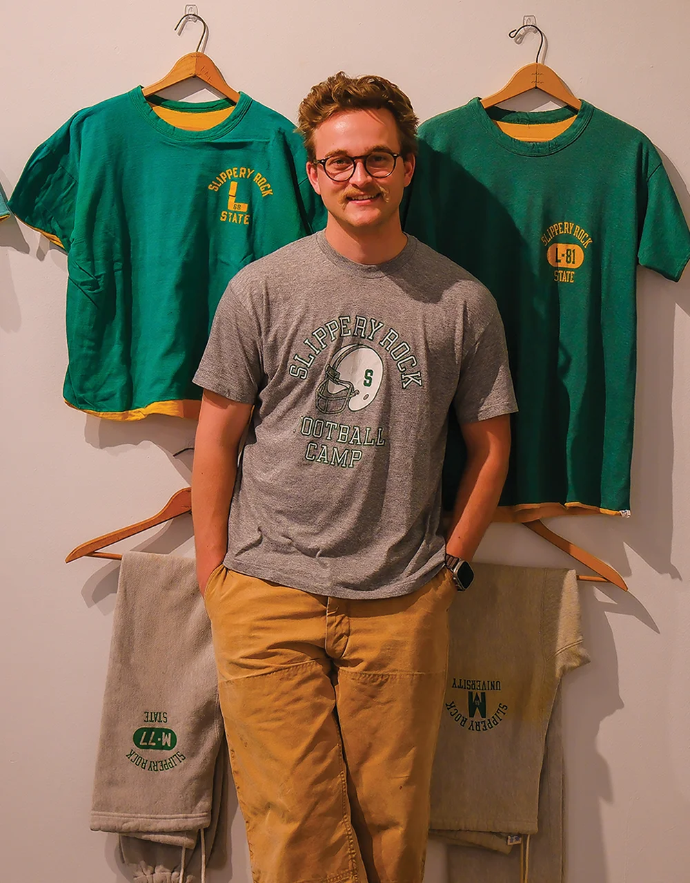 Aaron Fry standing in front of vintage Slippery Rock gear hanging on a wall