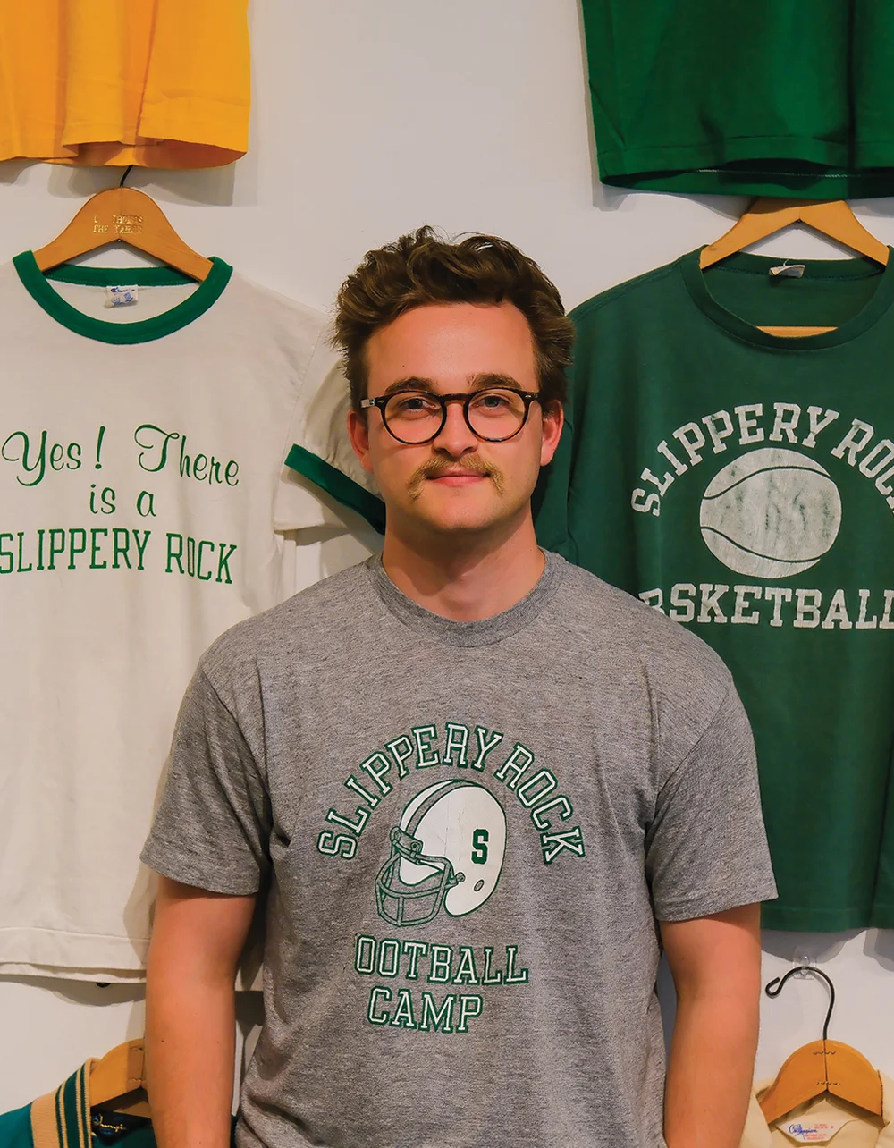 Aaron Fry standing in front of vintage Slippery Rock t-shirts hanging on a wall