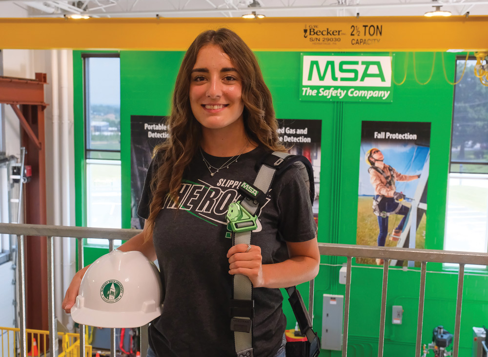 Shayla Wilkinson holding a white hard hat and a bag strapped to her shoulder