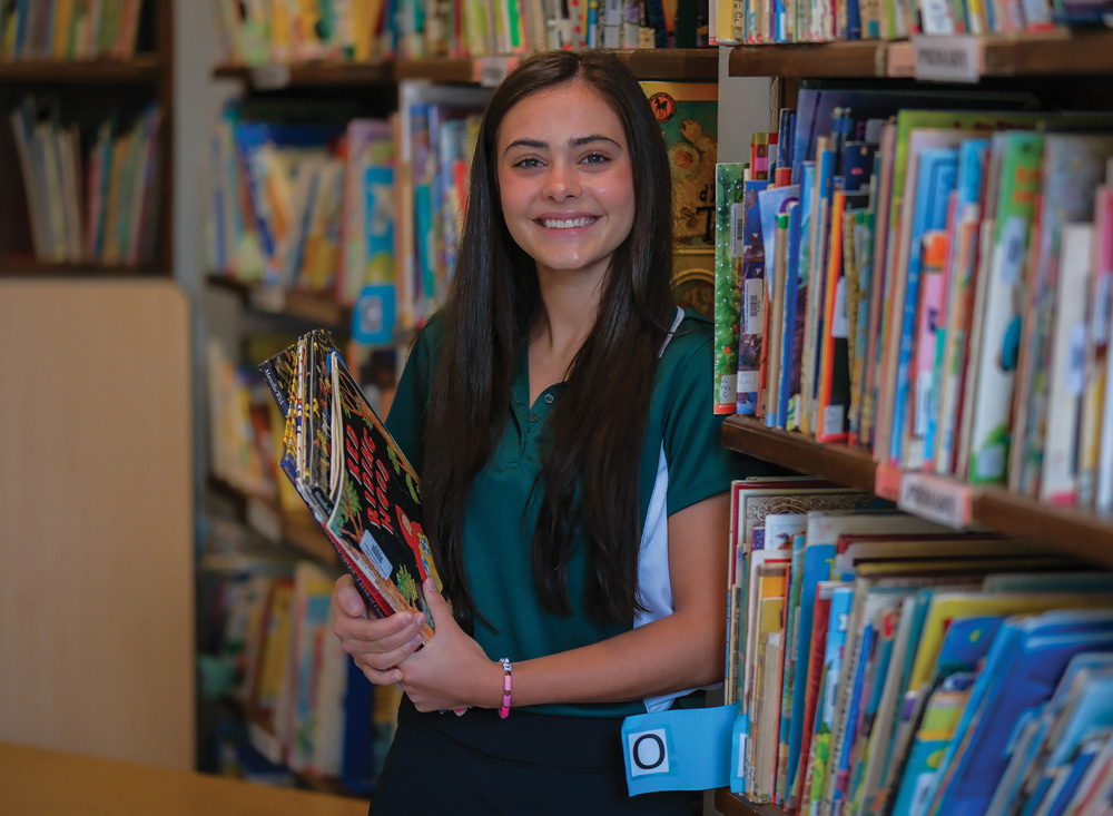 Abbey Stella in the kids section of a library, holding a stack of books