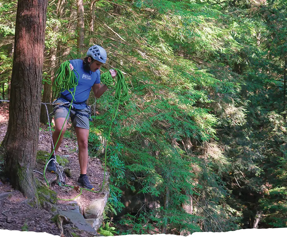 Alex Witmer standing at the top of a cliff holding rope for climbing