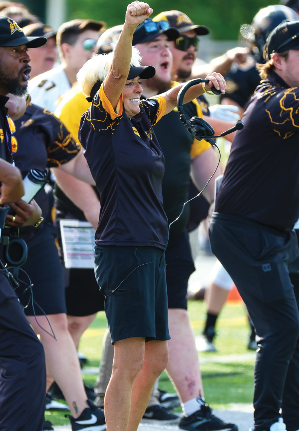 Teresa Conn holding her head set and raising her arms with a smile on her face while coaching for the Pittsburgh Passion