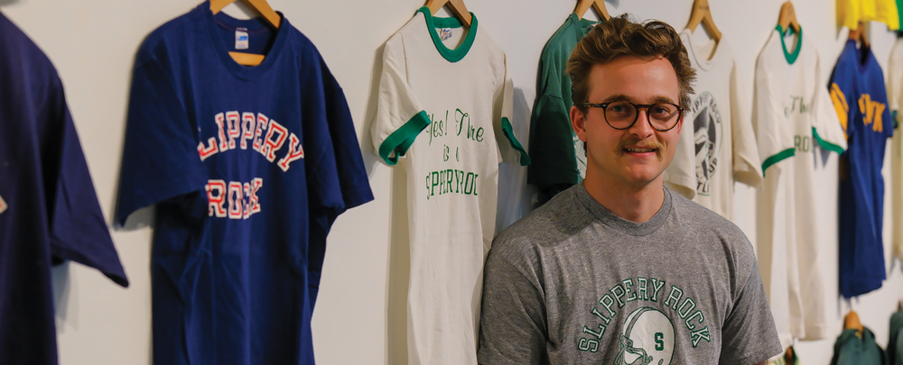 Aaron Fry standing in front of vintage Slippery Rock t-shirts hanging on a wall