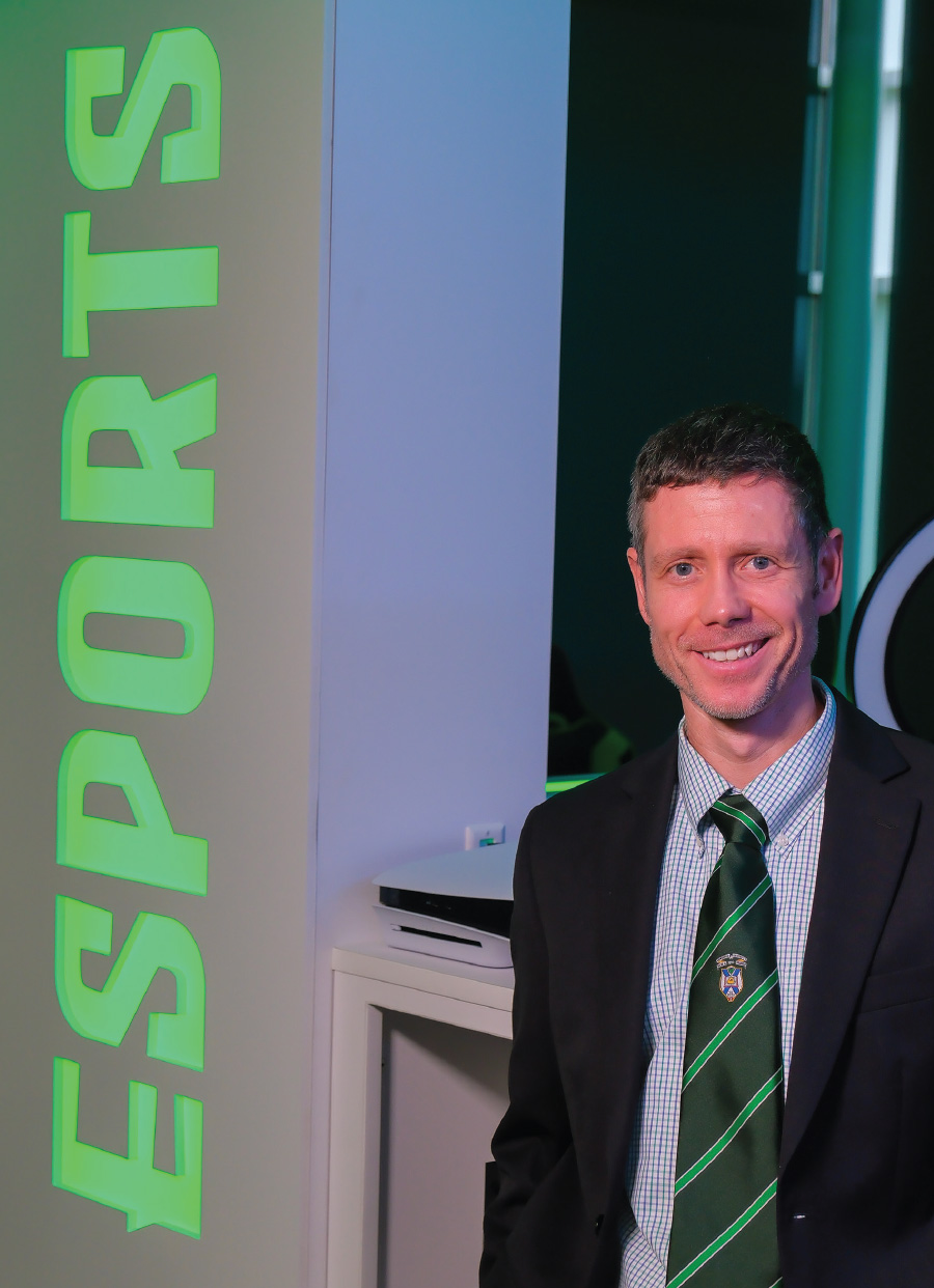 Seth Jenny in green striped tie and black suit jacket while standing in front of Esports backlit wall logo