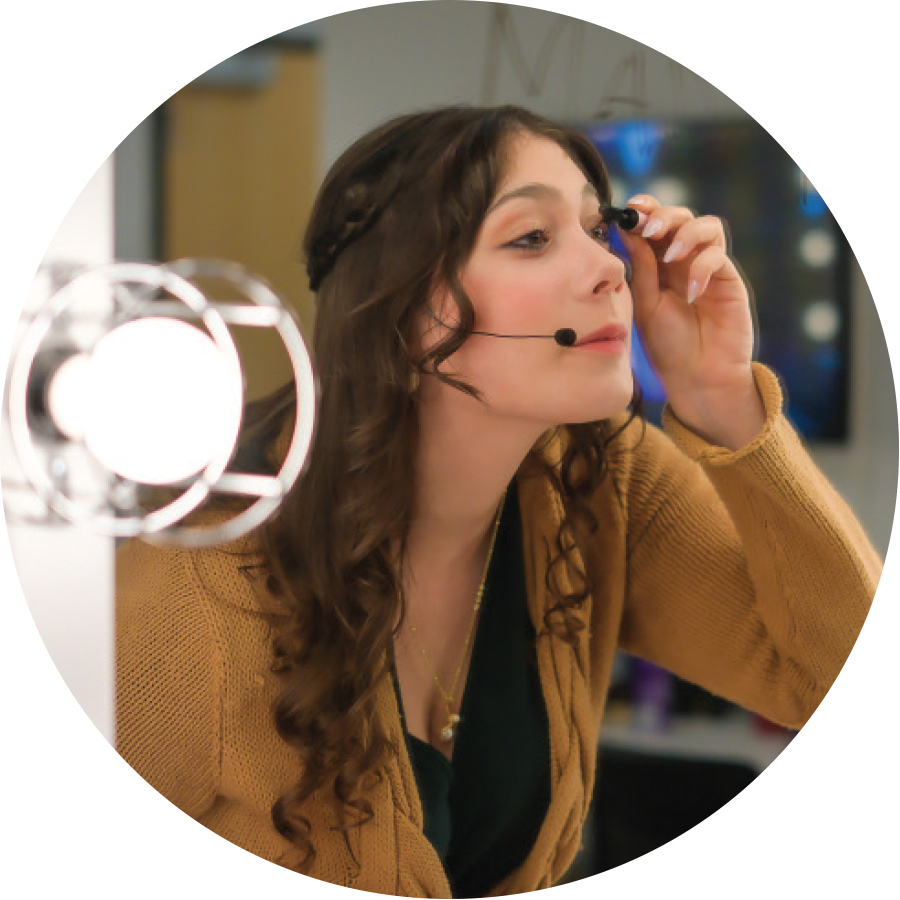 actress with headset microphone looking into mirror putting on mascara