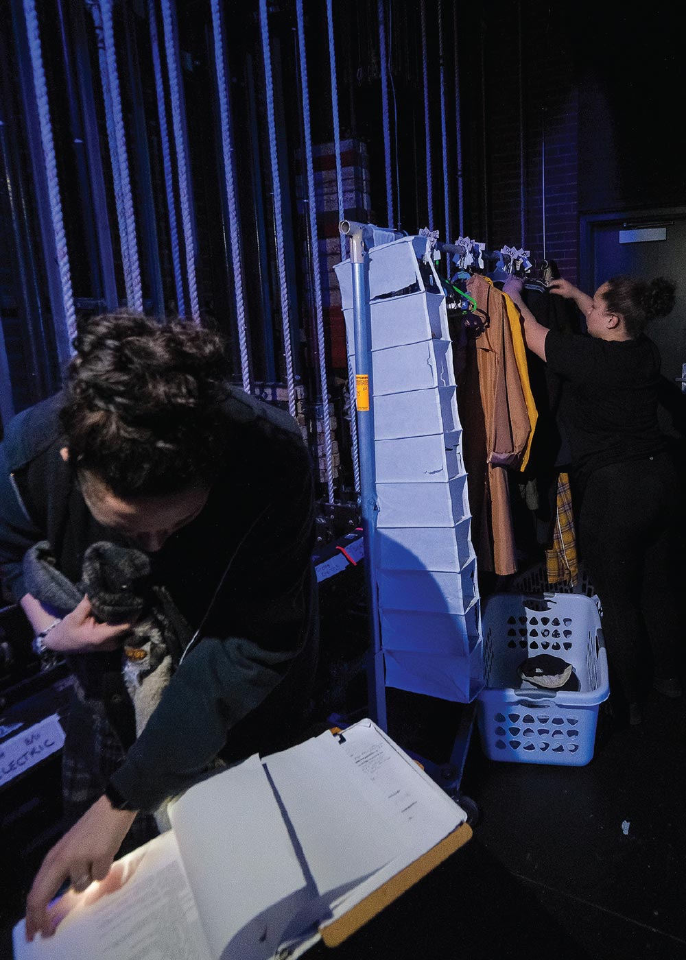 Stage crew members following the script backstage and pulling labeled costumes