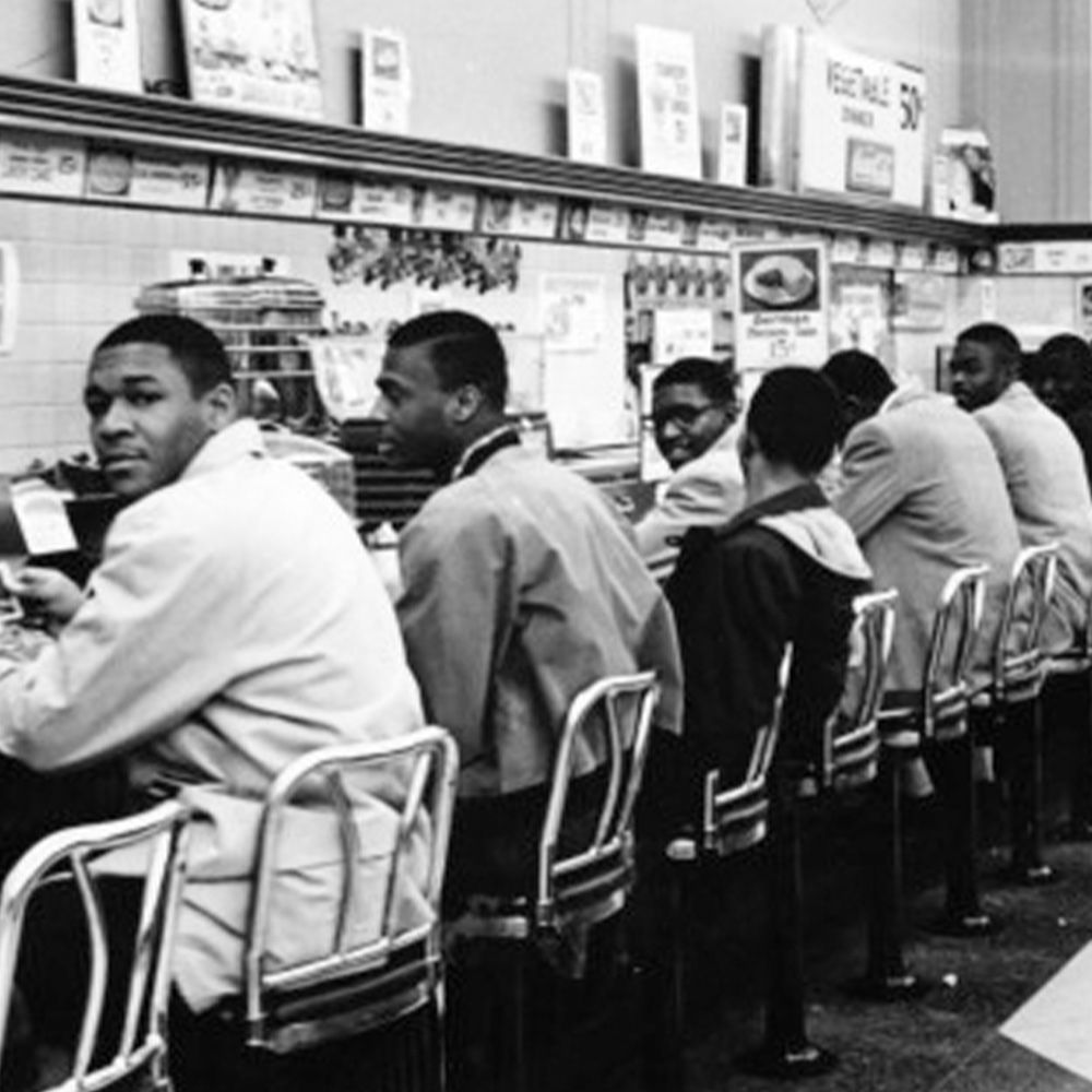 cropped black and white image of a group of young black men sitting at a diner counter