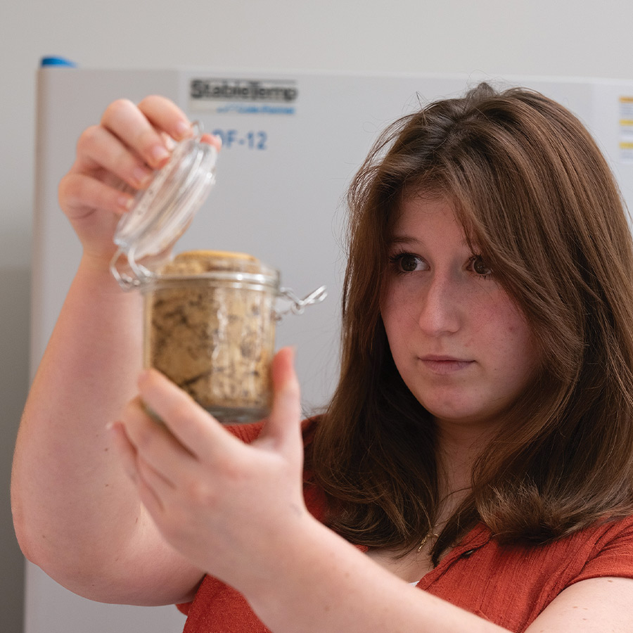 student Ashley Rimmel surveys sludge from an acid mine in a jar she hold at eye level