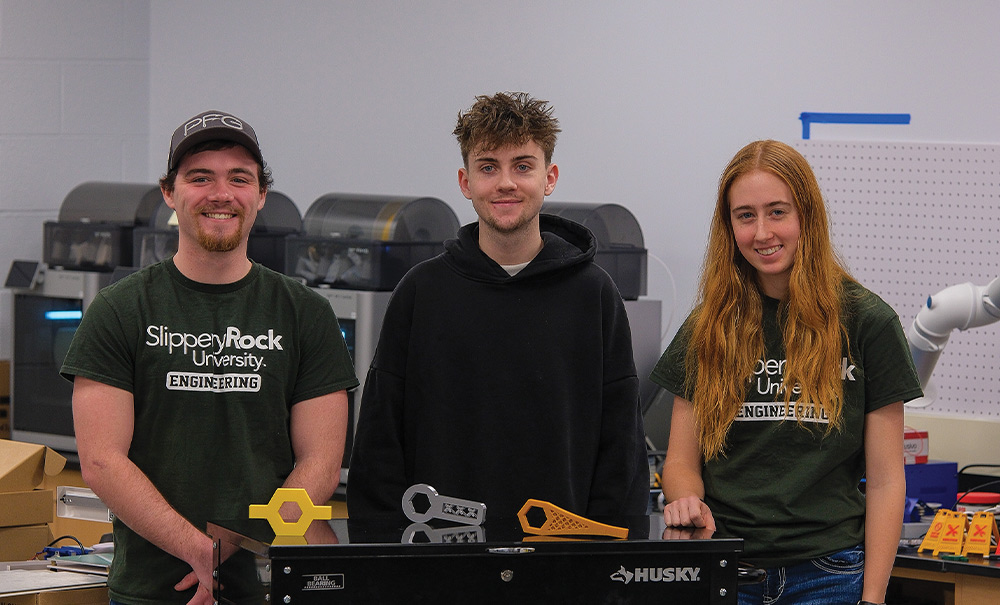 From left, Alexander Vollmer, Michael Rozic and Jennifer Cichra smile while standing in front of a rolling tool box displaying their 3D printed wrenches