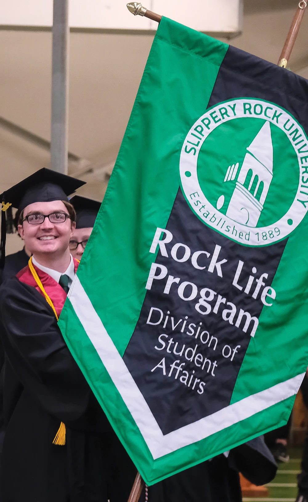 Person in graduation attire holding a "Rock Life Program" banner.