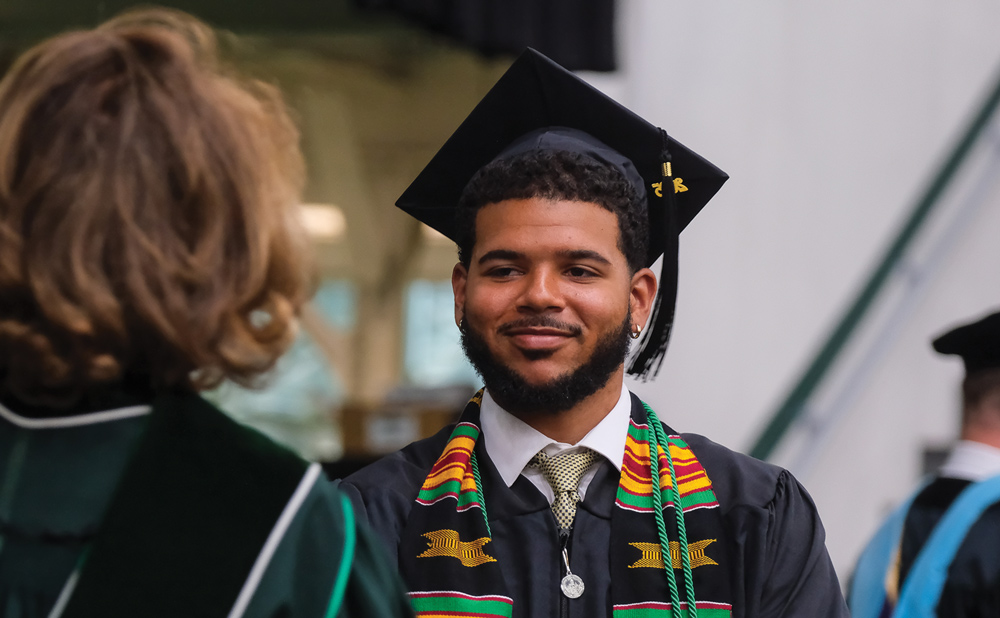 Young man in graduation attire smiling at an official.