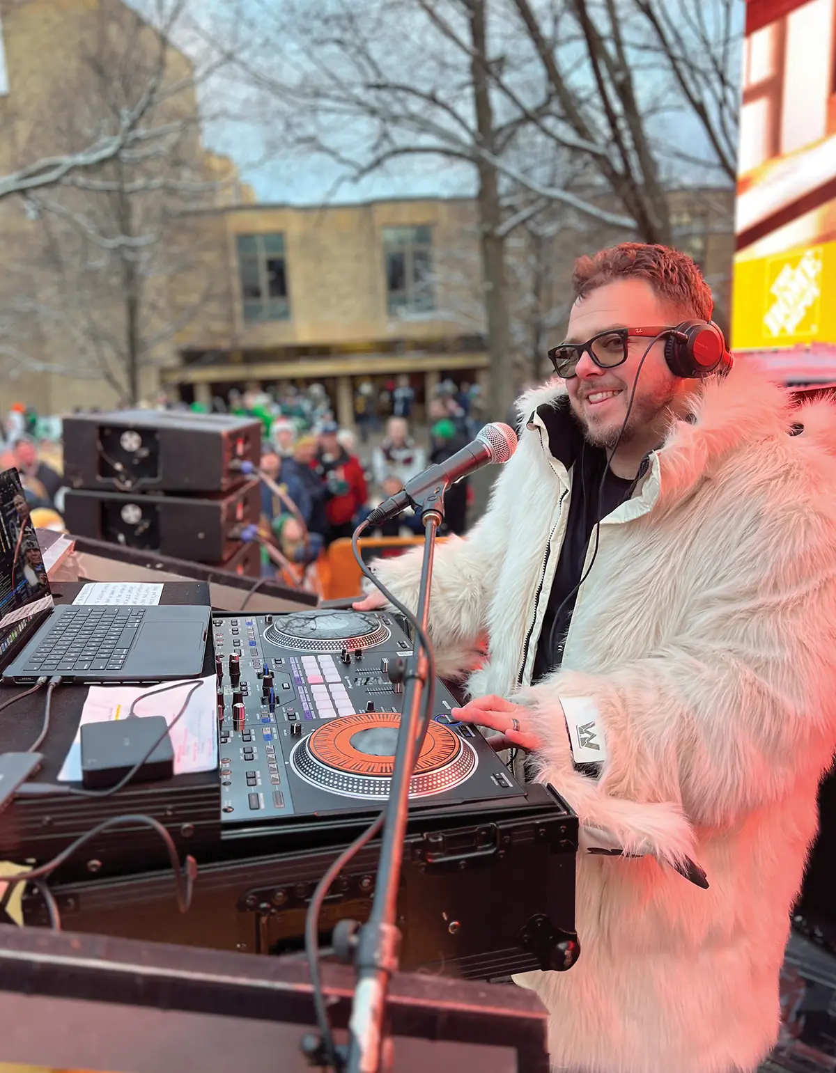 Ryan Griffin wearing a white fur coat and smiling in front of a turntable set at a college game day