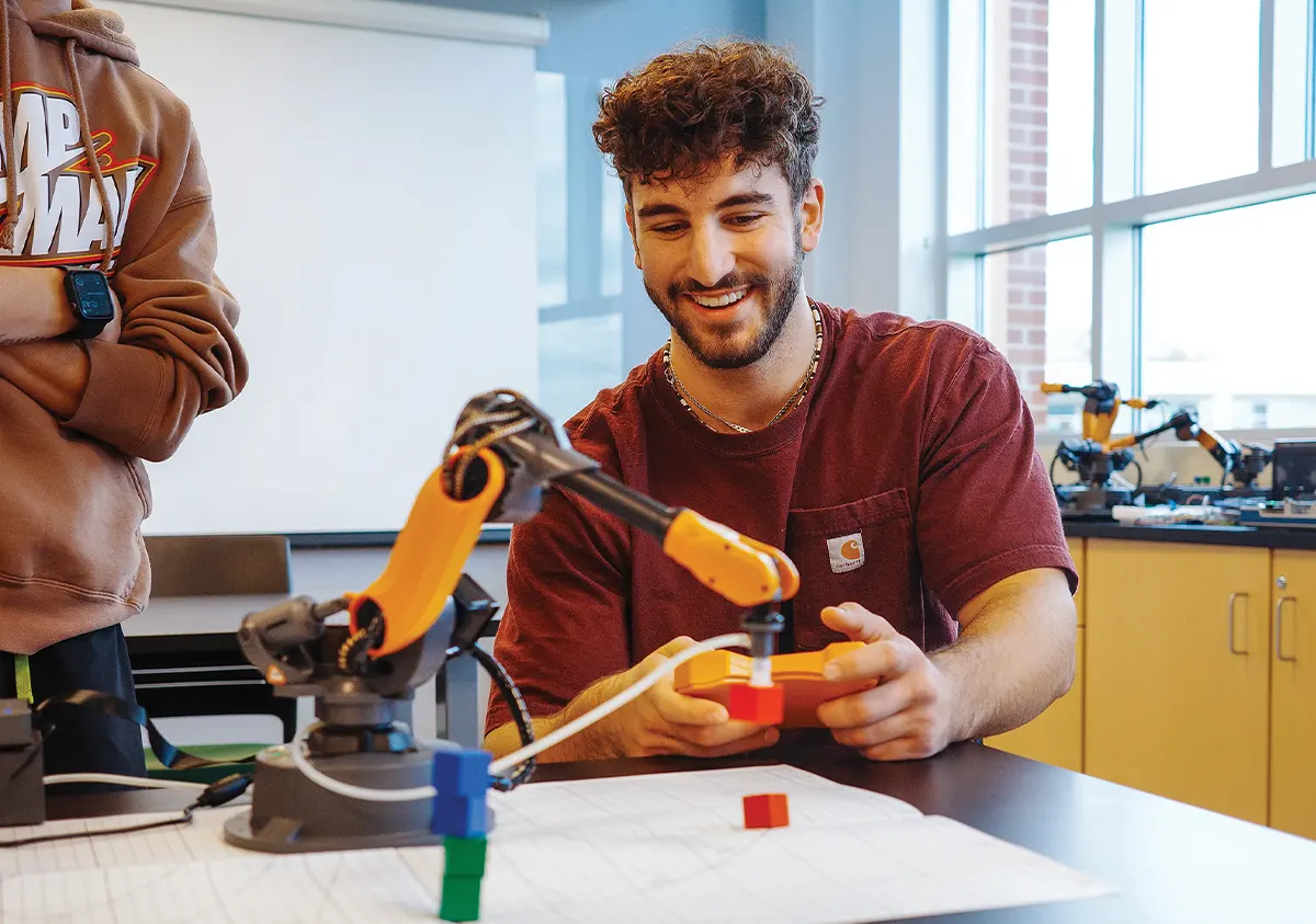 student using a remote controller to direct a robot arm to move small colorful blocks