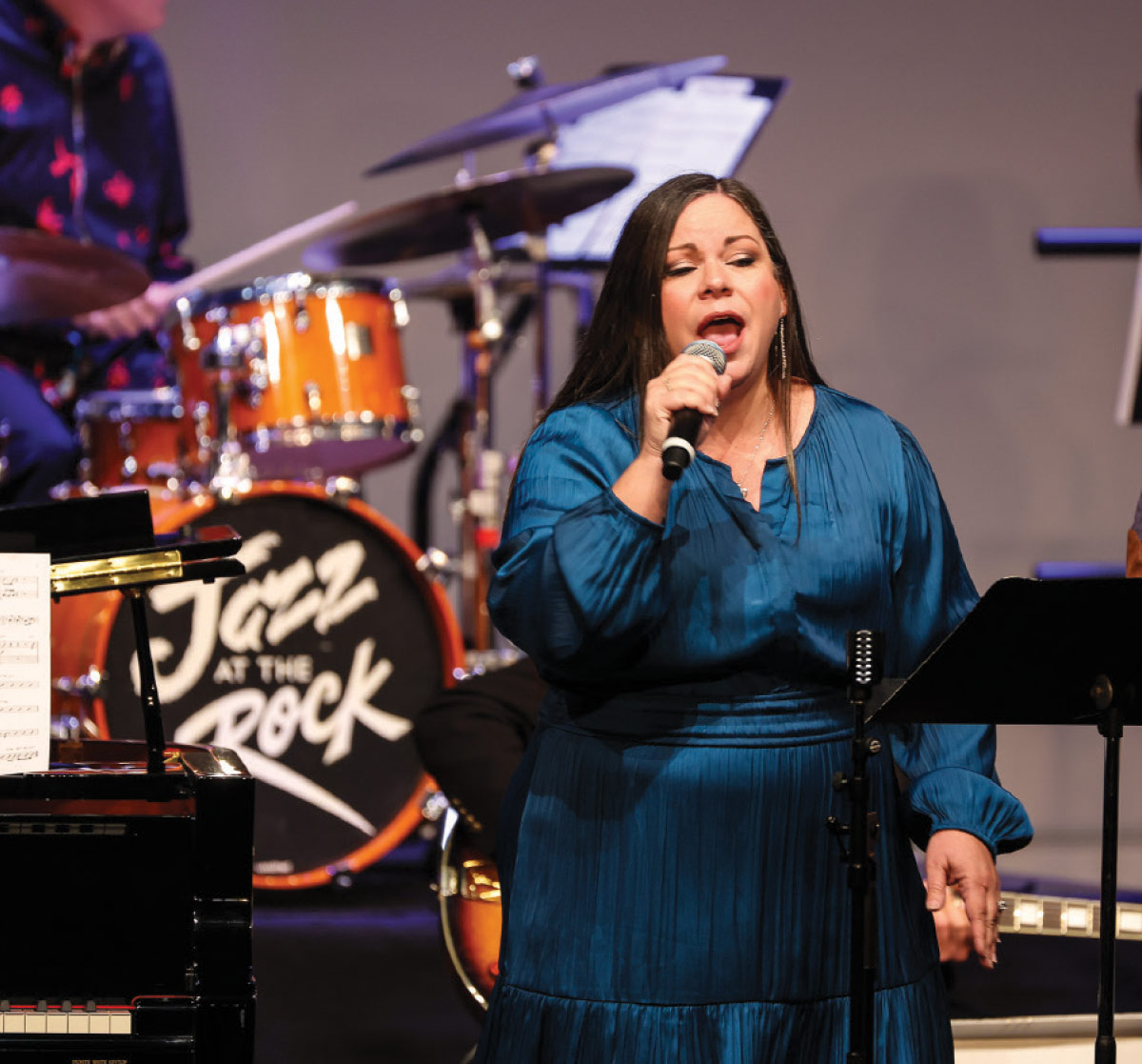A woman in a blue satin dress sings into a microphone.