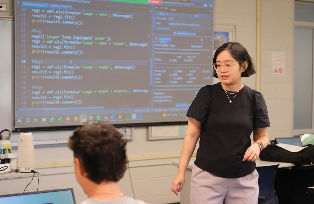 Xintong Wang stands in front of a screen displaying Python code.