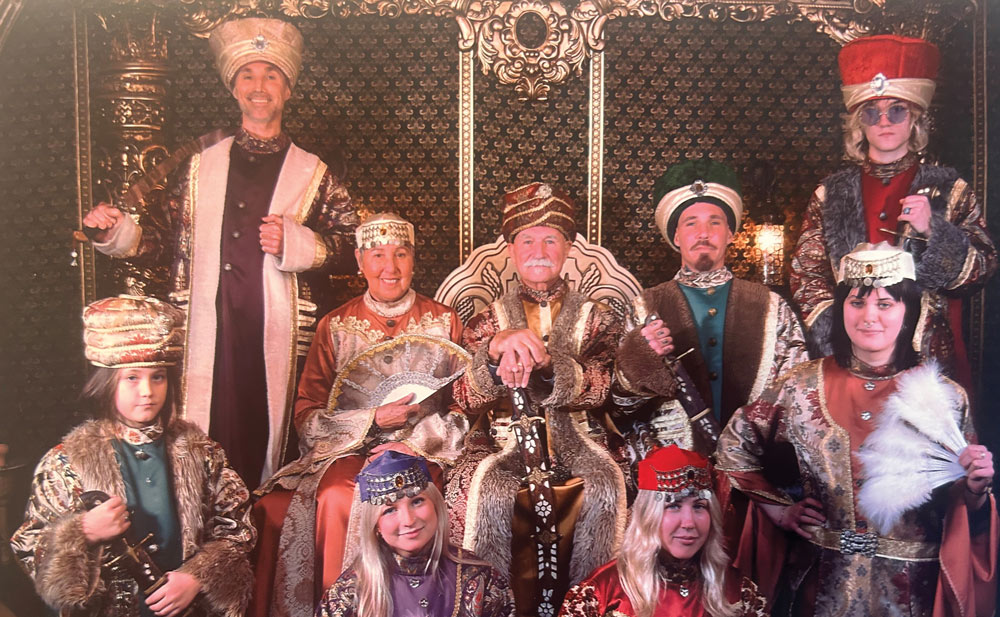 A group in medieval royal attire posing in an ornate setting.