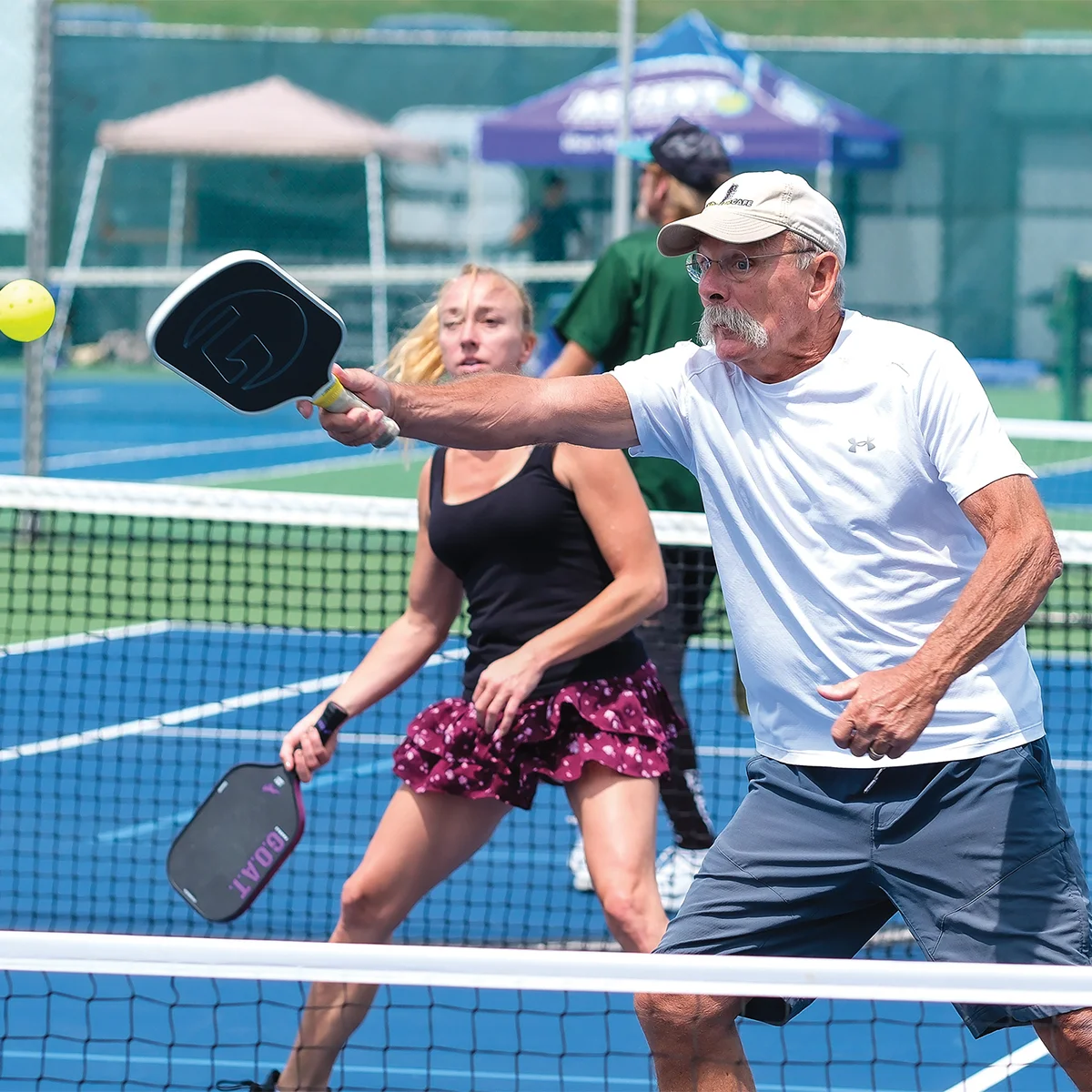 Two pickleball players focused on the yellow ball above the net during a recreational or competitive tournament.