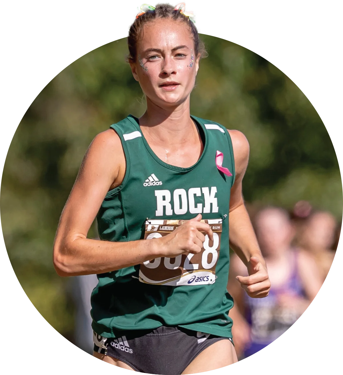Young woman competing in a distance running event, wearing athletic gear and a pink awareness ribbon pinned to her shirt.