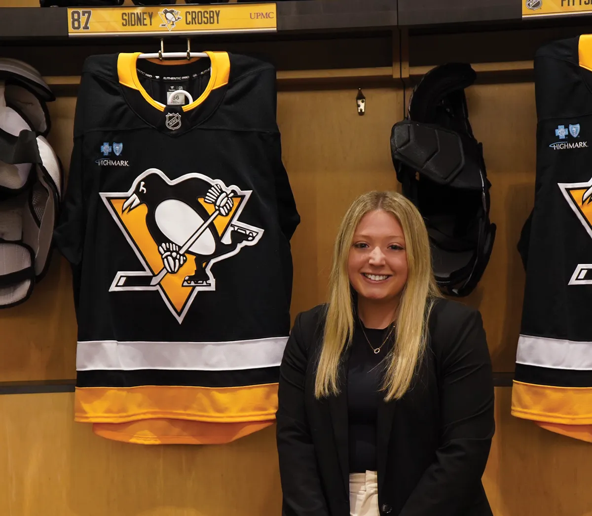 Bailey Kuhn standing in front of an NHL locker displaying a Sidney Crosby Pittsburgh Penguins jersey.