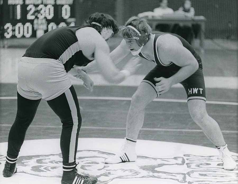 Archival black and white photo of two college wrestlers facing off on a mat.