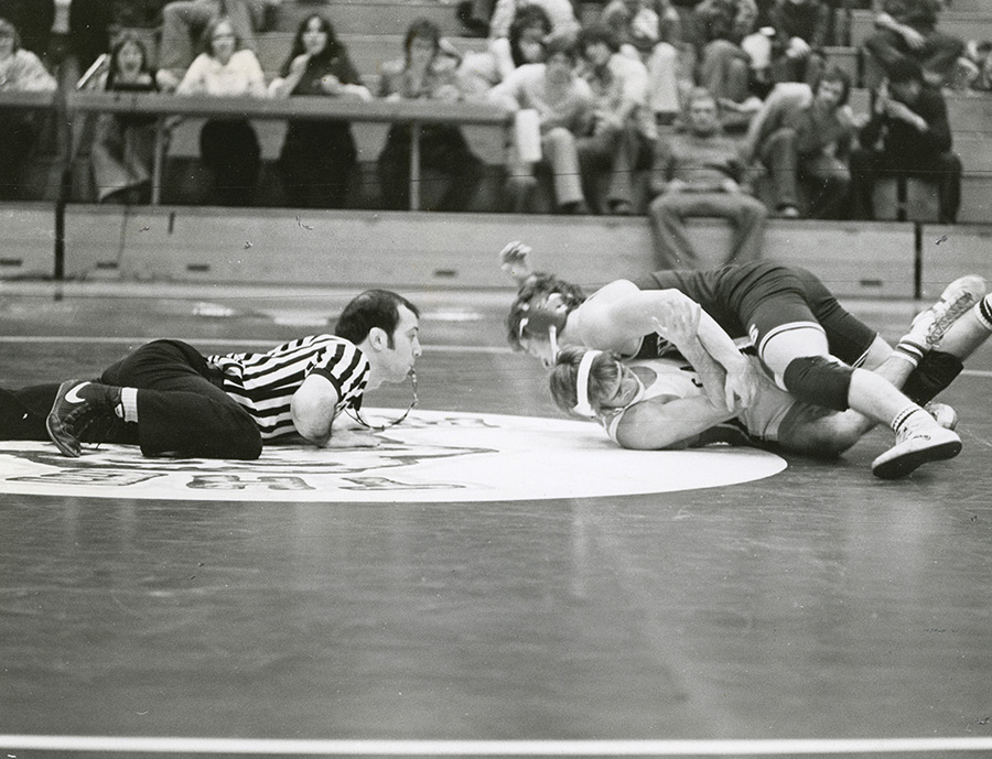Vintage photo of a referee watching closely as two wrestlers grapple on the mat.