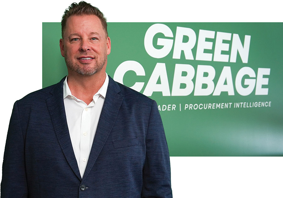 Eric Cunningham stands in a dark blue blazer and white dress shirt in front of a green "GREEN CABBAGE" sign.