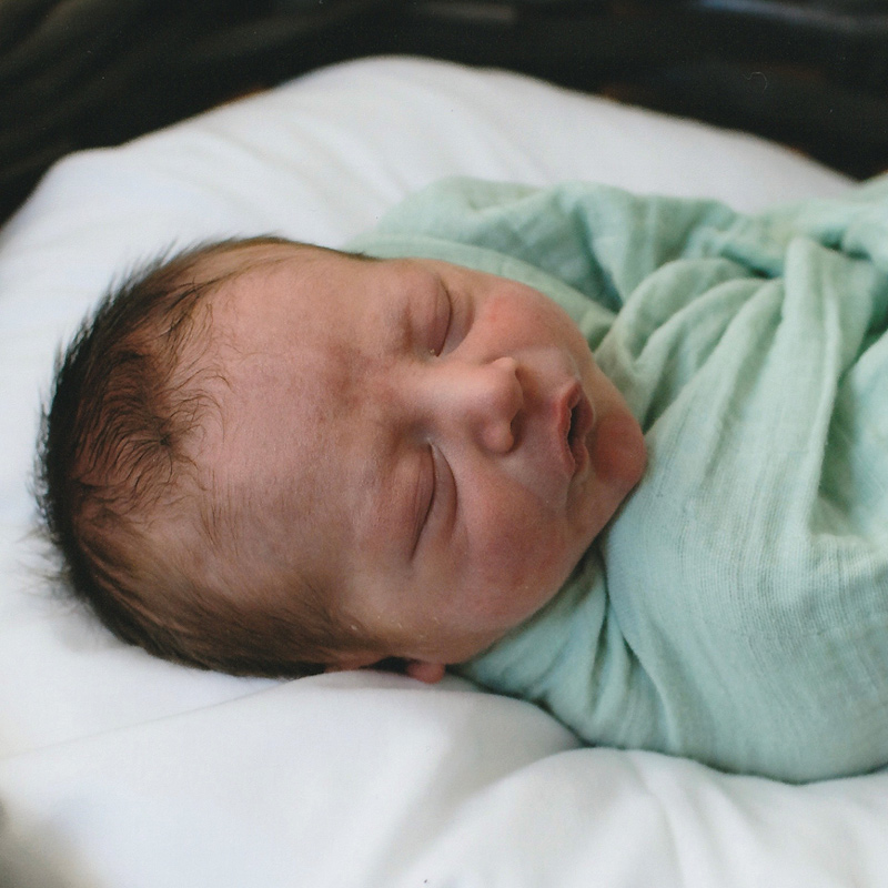 A close-up view of a newborn baby sleeping peacefully while wrapped snugly in a light green swaddle blanket.