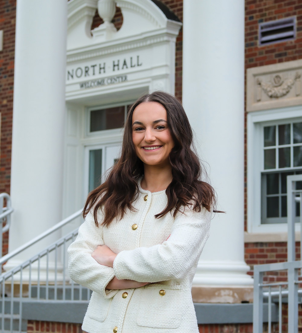 A smiling woman with arms crossed poses outside in front of the Slippery Rock North Hall building entrance.