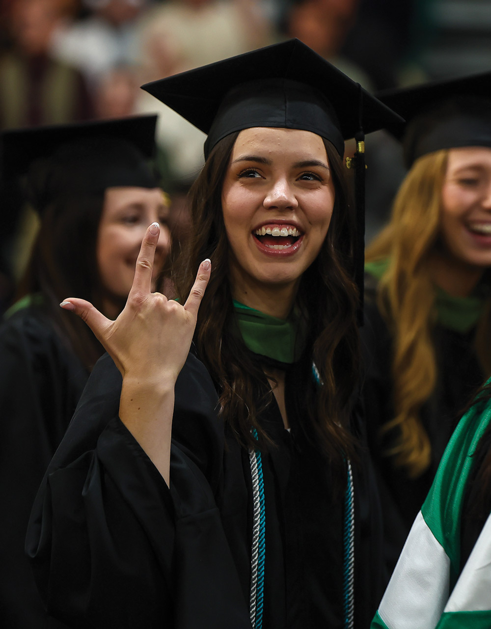Smiling graduate in a black cap and gown holds up a hand sign celebrating during a Slippery Rock ceremony.