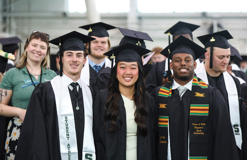 Three Slippery Rock graduates in caps and gowns smile for a group portrait at a commencement ceremony.