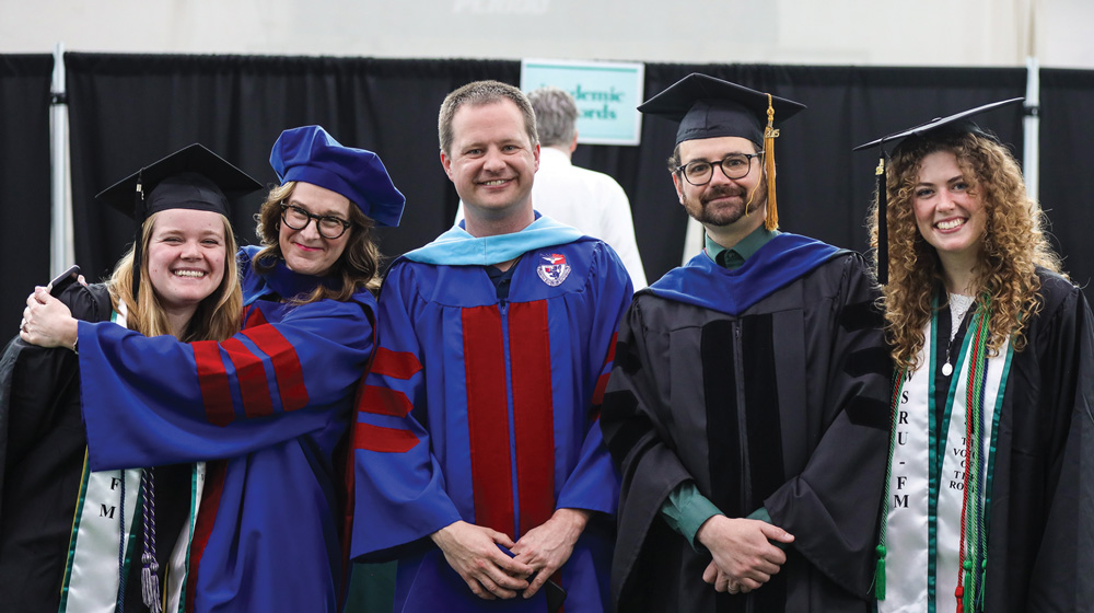 Five smiling Slippery Rock faculty members and graduates pose together in academic regalia.
