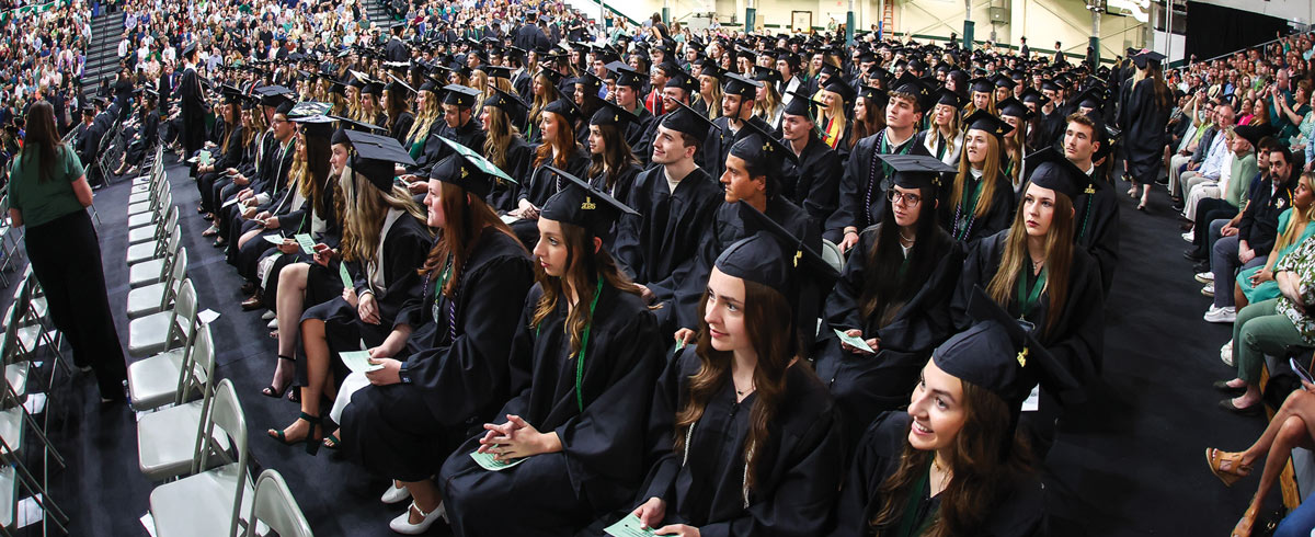 A high-angle view of rows of Slippery Rock graduates in caps and gowns seated during commencement.